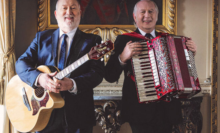 Two men, Foster and Allen, stand side by side, smiling, one holds an acoustic guitar, the other an accordion. Gold and white text above them reads 'Foster & Allen', 'We'll Meet Again', 'Irish Tour'.